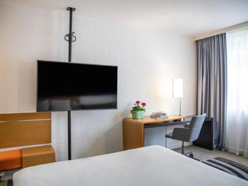 a hotel room with a bed and a desk and a tv at Hotel Novotel Evry Courcouronnes in Evry-Courcouronnes
