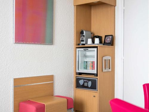a room with a shelf with a microwave and red chairs at Hotel Novotel Evry Courcouronnes in Evry-Courcouronnes