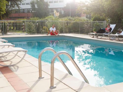two women sitting in chairs by a swimming pool at Hotel Novotel Evry Courcouronnes in Evry-Courcouronnes