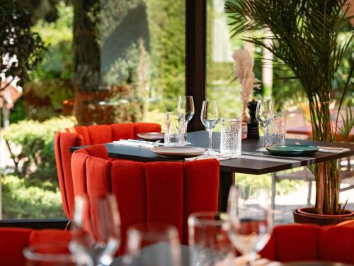 a table with wine glasses and red chairs in front of a window at Novotel Aix-en-Provence Pont de L'Arc in Aix-en-Provence