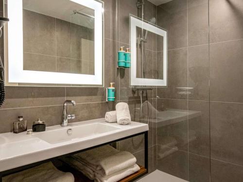un bagno con lavandino, specchio e doccia di Novotel Antibes Sophia Antipolis a Valbonne