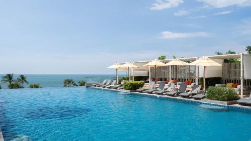 a swimming pool with chairs and umbrellas and the ocean at Holiday Inn Pattaya by IHG in Pattaya Central