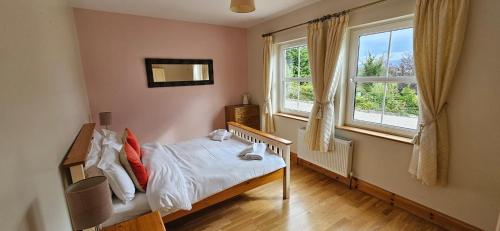 a small bedroom with a bed and two windows at Charming Coastal Cottages by Portsalon Beach in Portsalon