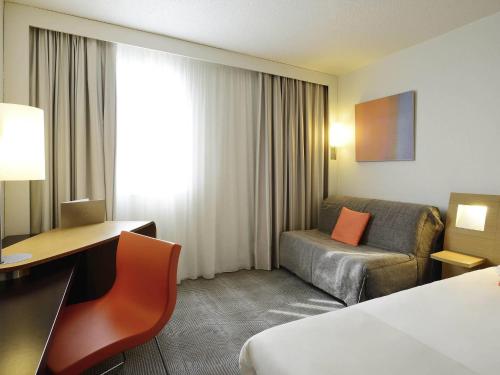 a hotel room with a bed and a desk and a chair at Novotel Chartres in Chartres