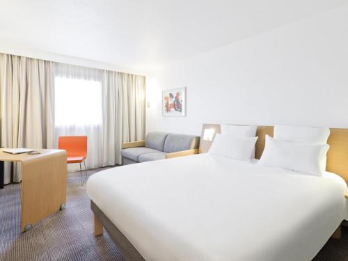 a hotel room with a large bed and a chair at Novotel Pau Pyrénées in Lescar