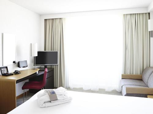 a hotel room with a desk and a bed at Novotel Pau Pyrénées in Lescar