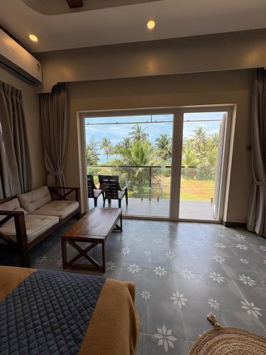 a bedroom with a bed and a living room with a large window at Karkera's Beach Stay in Malpe