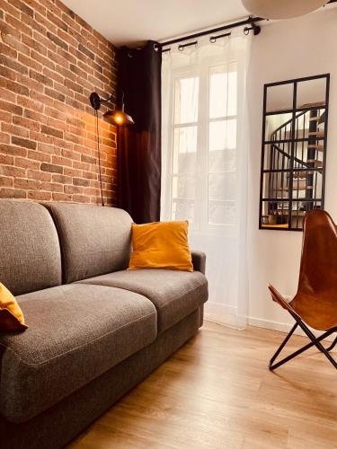 a living room with a couch and a brick wall at Gites les Pourquoi Pas - Résidence de Tourisme DSV Bayeux in Bayeux