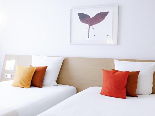 two beds with colorful pillows in a hotel room at Novotel Reims Tinqueux in Reims