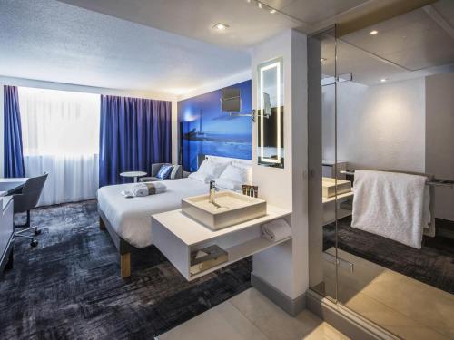 a hotel room with a bed and a sink and a shower at Novotel Rennes Alma in Rennes