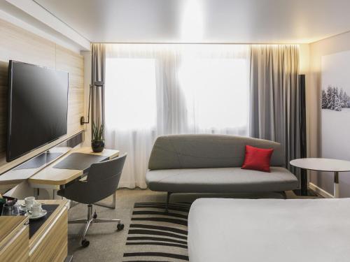 a hotel room with a couch and a television at Novotel Strasbourg Centre Halles in Strasbourg