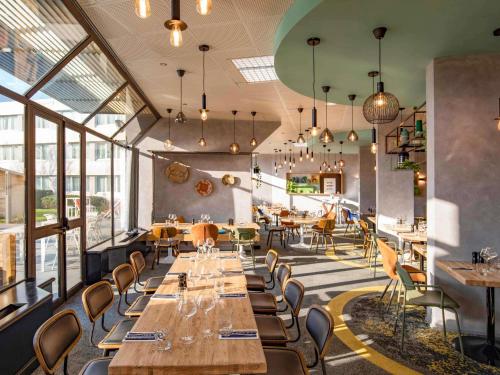 a restaurant with wooden tables and chairs and windows at Novotel Le Mans in Le Mans