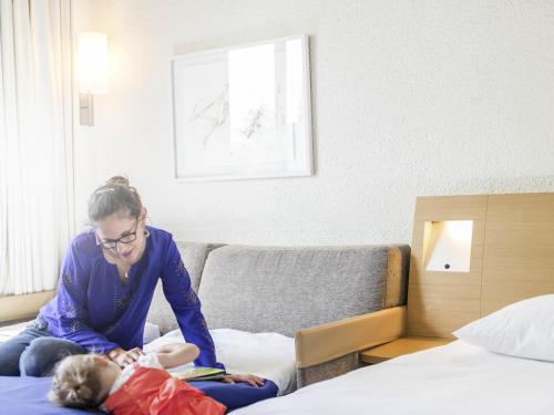 a woman sitting on a bed reading a book to a child at Novotel Le Mans in Le Mans