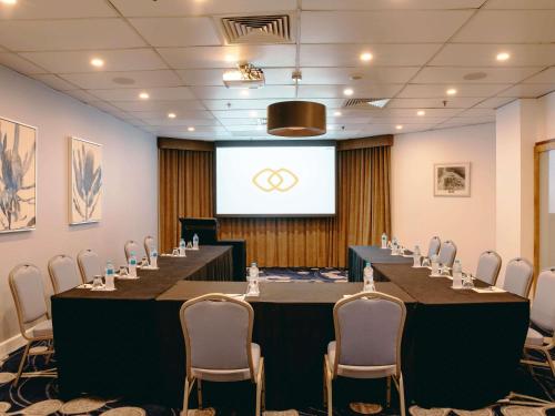 a conference room with a long table and chairs and a screen at Sofitel Gold Coast Broadbeach in Gold Coast