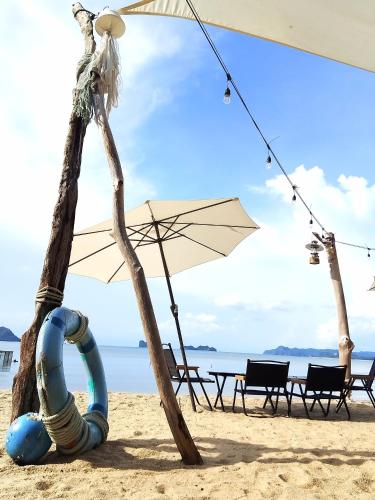 a beach with an umbrella and chairs on the sand at Aura Bluewave Beach House and Mini Beach Cafe in Tanjung Rhu 