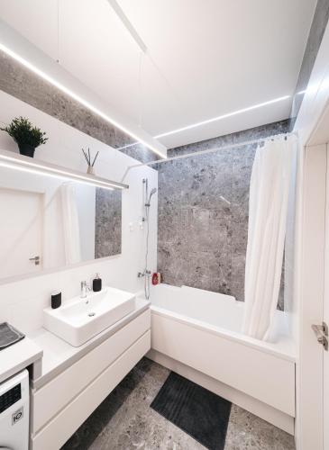 a white bathroom with a tub and a sink at Cozy Dzintaru apartment - Steps from Forest and Sea in Jūrmala