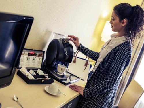 a woman standing at a desk with a coffee maker at Mercure Hotel Berlin City West in Berlin