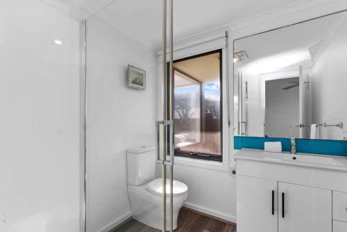 Un baño blanco con inodoro y ventana. en Blue Sea - Beachfront Escape, en Apollo Bay