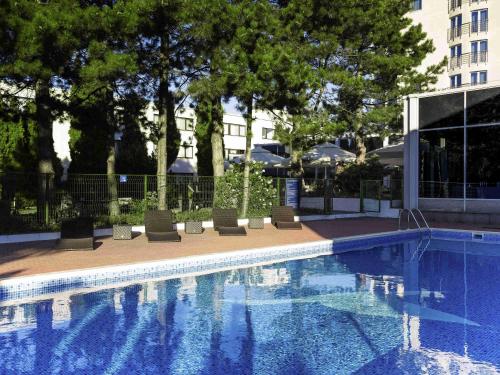 a swimming pool with chairs and trees and a building at Novotel Warszawa Airport in Warsaw