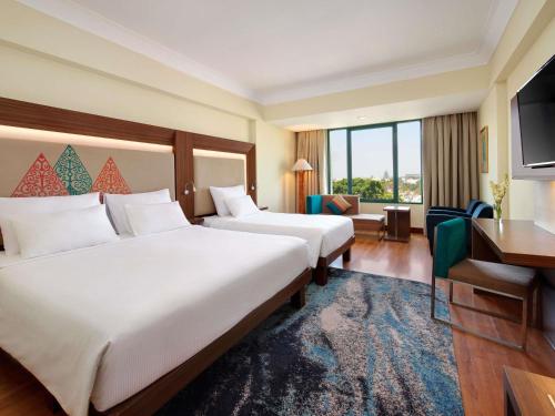 a hotel room with two beds and a desk at Novotel Solo in Solo
