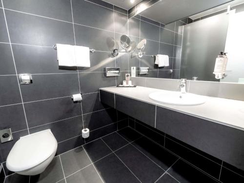 a bathroom with a toilet and a sink and a mirror at Mercure Bordeaux Lac in Bordeaux