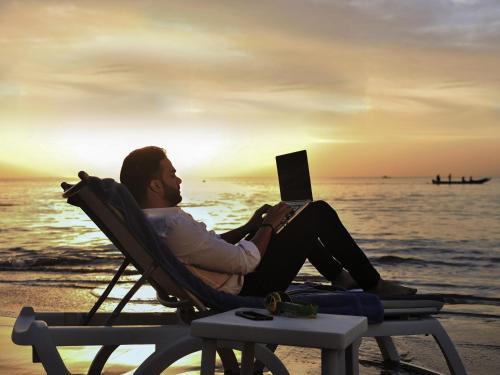 a man sitting in a chair on the beach with a laptop at Pullman Dakar Teranga in Dakar