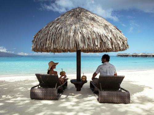 a man and woman sitting under an umbrella on a beach at Sofitel Kia Ora Moorea Beach Resort in Maharepa