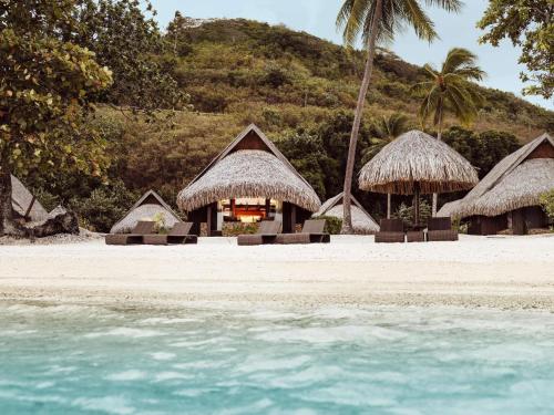 a group of huts on a beach with the water at Sofitel Kia Ora Moorea Beach Resort in Maharepa