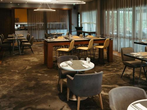a dining room with tables and chairs and windows at Pullman Toulouse in Blagnac