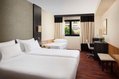 a hotel room with two beds and a desk at NH Ciudad de Valencia in Valencia