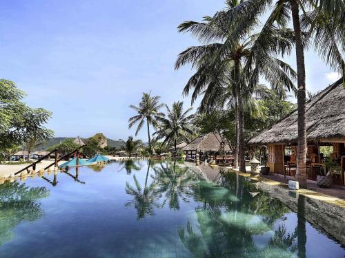 a swimming pool with palm trees and a resort at Novotel Lombok Resort & Villas in Kuta Lombok
