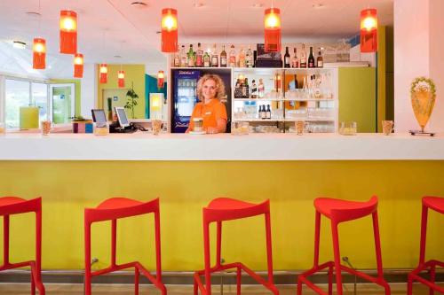 a woman standing behind a bar with red stools at ibis Styles Duesseldorf-Neuss in Neuss
