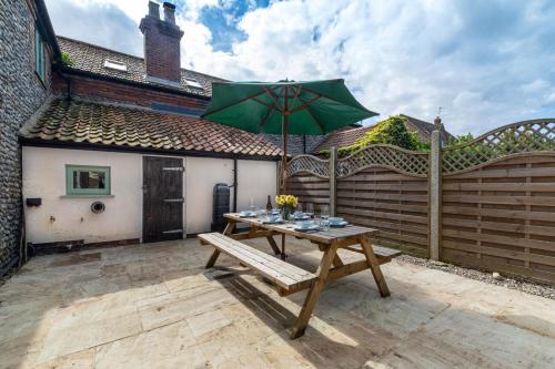 a wooden table with a green umbrella on a patio at Warborough House East in Kelling