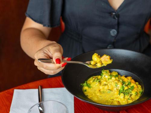 a person holding a spoon and a pan of food at ibis Carcassonne Est la Cité in Carcassonne