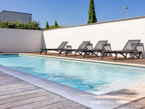 a swimming pool with lounge chairs next to a wall at ibis Carcassonne Est la Cité in Carcassonne