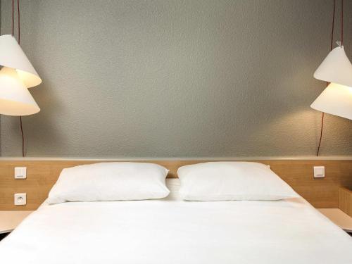 a bed with two pillows in a room with two lights at ibis Montélimar Nord in Saulce-sur-Rhône