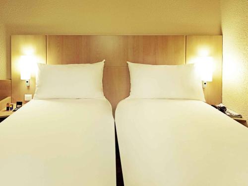 two beds in a hotel room with white sheets and pillows at ibis Nemours in Nemours