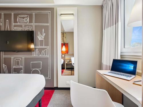 a room with a bed and a desk with a laptop at ibis Paris Porte D'Orleans in Montrouge