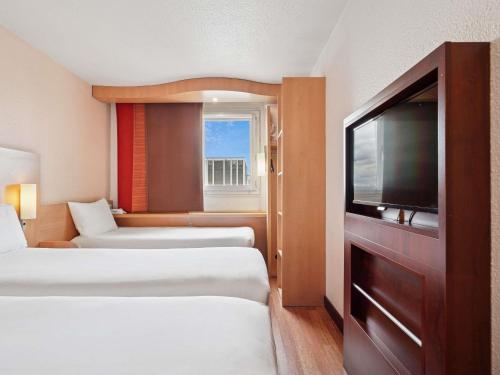 a hotel room with two beds and a flat screen tv at ibis Paris Porte D'Orleans in Montrouge