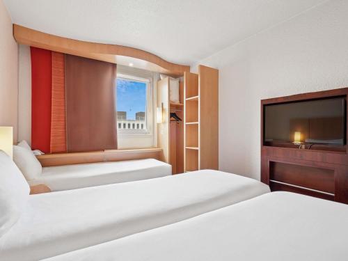 a hotel room with two beds and a flat screen tv at ibis Paris Porte D'Orleans in Montrouge