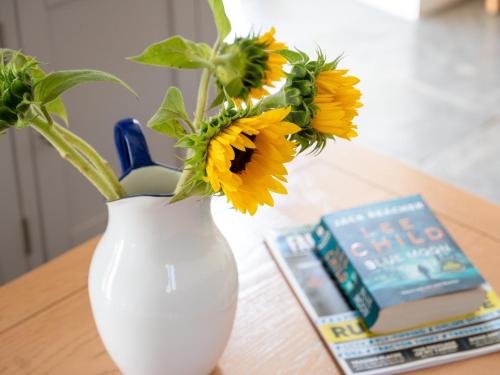 a white vase with sunflowers on a table next to a book at 2 Bed in Chulmleigh 72791 in Coldridge