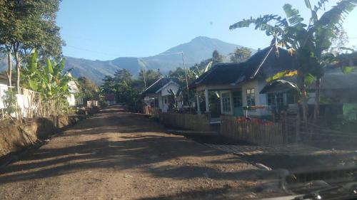 a dirt road with houses and mountains in the background at Tetebatu Indah Homestay in Tetebatu