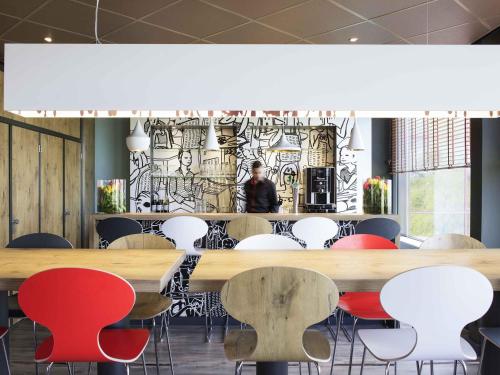 a room with tables and chairs and a man in the background at Ibis Schiphol Amsterdam Airport in Badhoevedorp