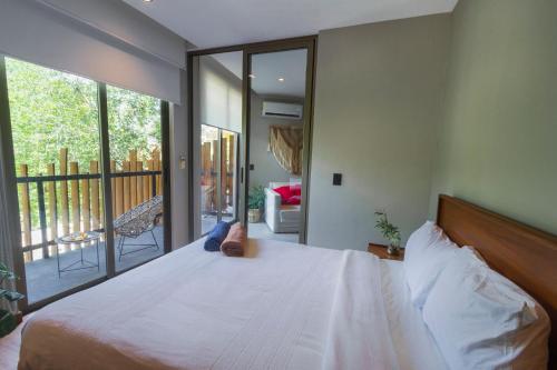 a bedroom with a white bed with a large window at Phimai, Tu Lugar Magico En Tulum in Tulum