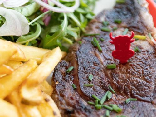 a steak with fries and a salad with a red devil toy on it at Hotel ibis Narbonne in Narbonne