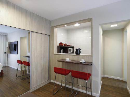 a room with a bar with red chairs and a kitchen at Mercure Sao Paulo Alamedas in Sao Paulo