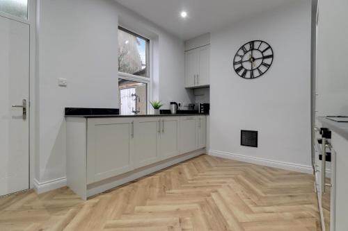 a kitchen with white cabinets and a clock on the wall at Luxury 2 Bed House in Lindley Huddersfield 2 mins from HRI 5 mins from Town Centre and M62 in Lindley