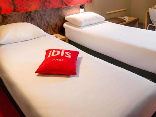 a hotel room with two beds with a red pillow at ibis Saint-Omer Centre in Saint-Omer