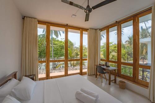 a bedroom with a bed and a desk and windows at Ko Lake Villa in Ahangama
