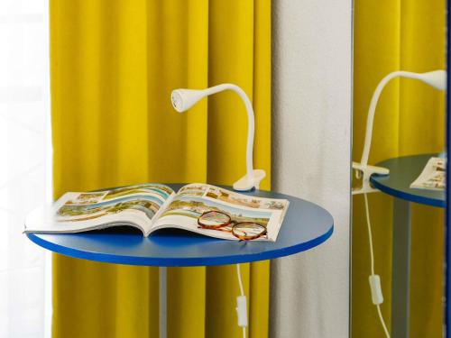 a book and glasses on a table with a lamp at ibis Styles Paris République Le Marais in Paris